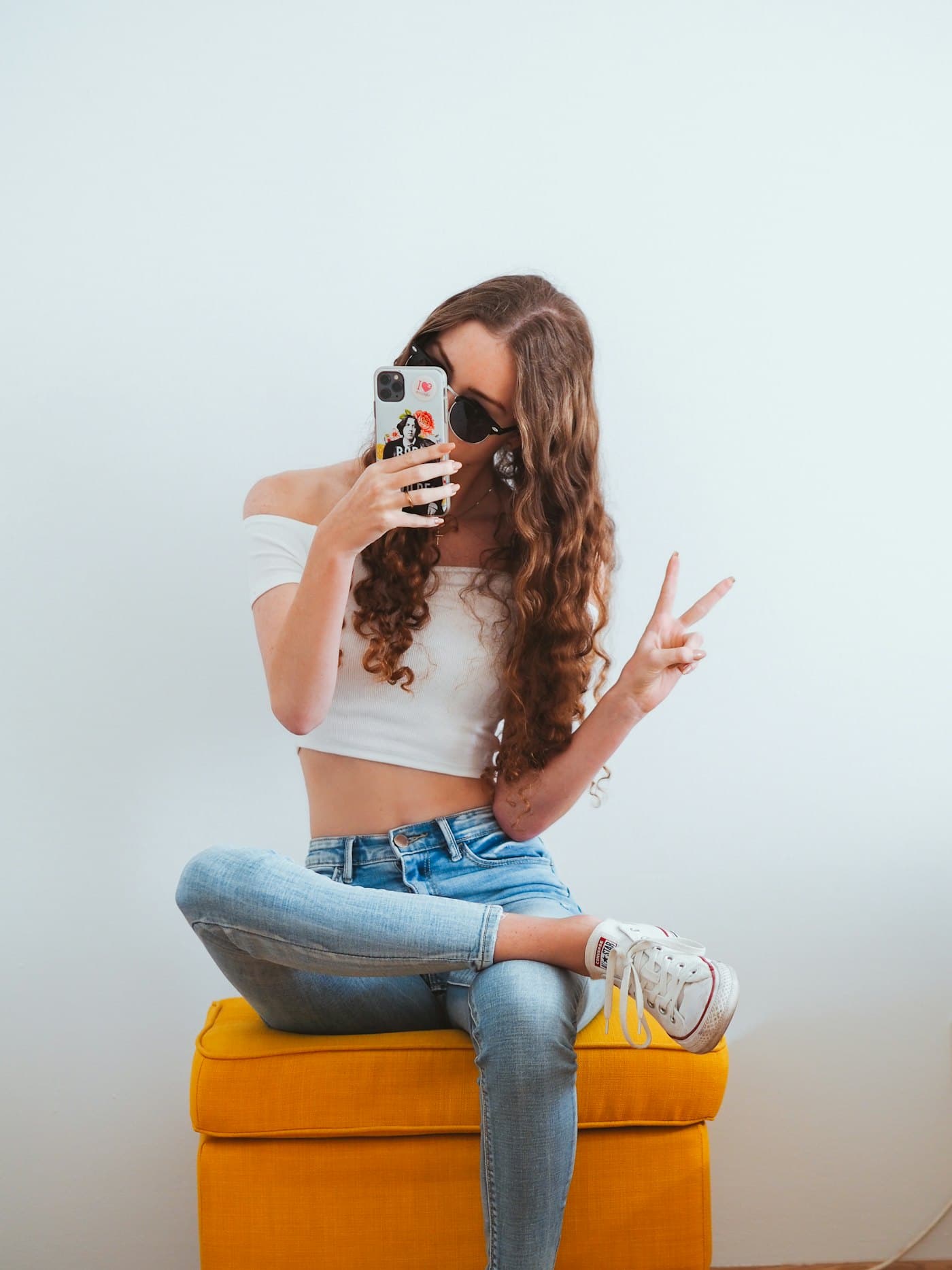 A creator sitting cross-legged taking a mirror selfie and making a peace sign